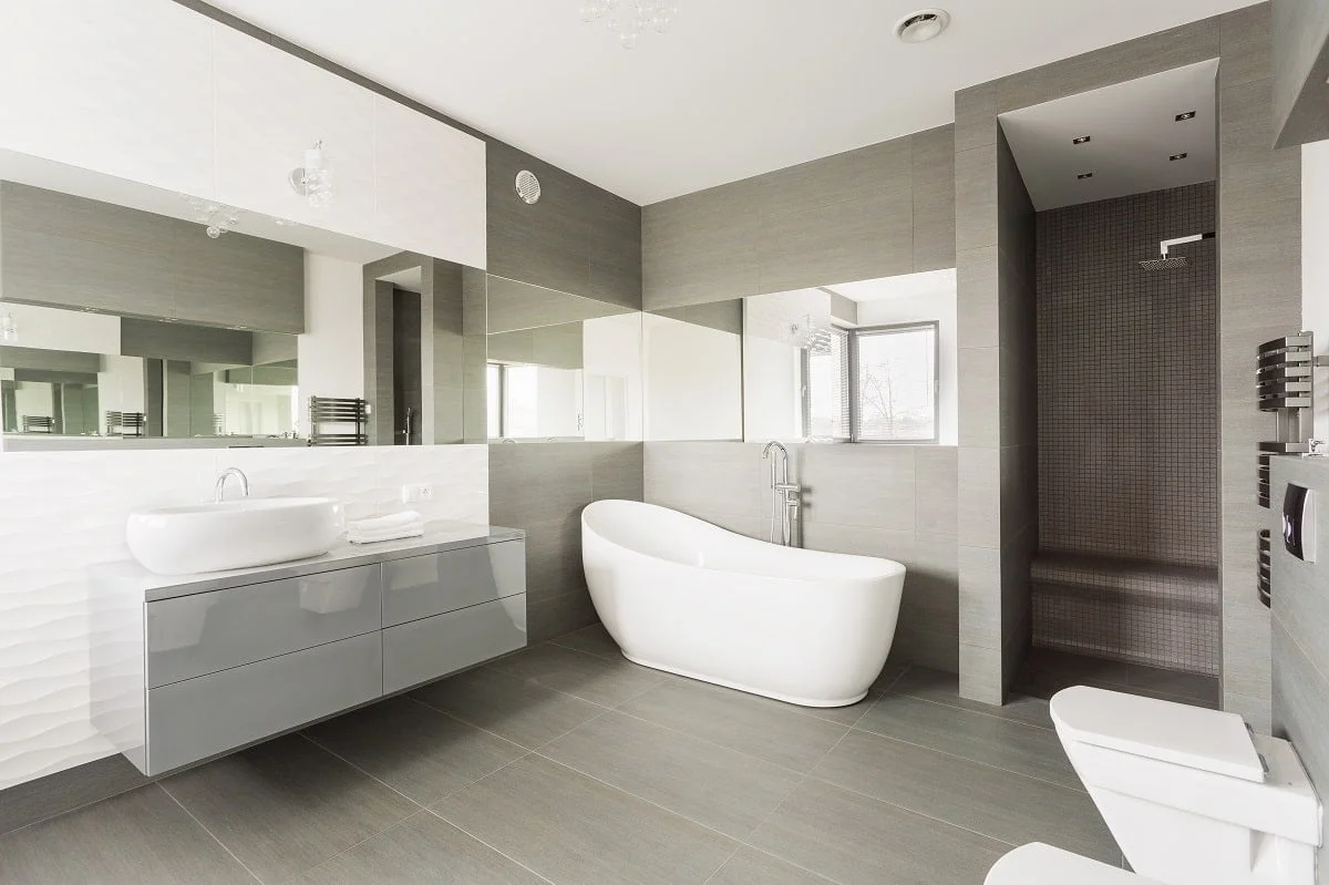 Helles Bad mit Badewanne, Toilette und Waschbecken in weiß und einer großen Spiegelfront und Regendusche.