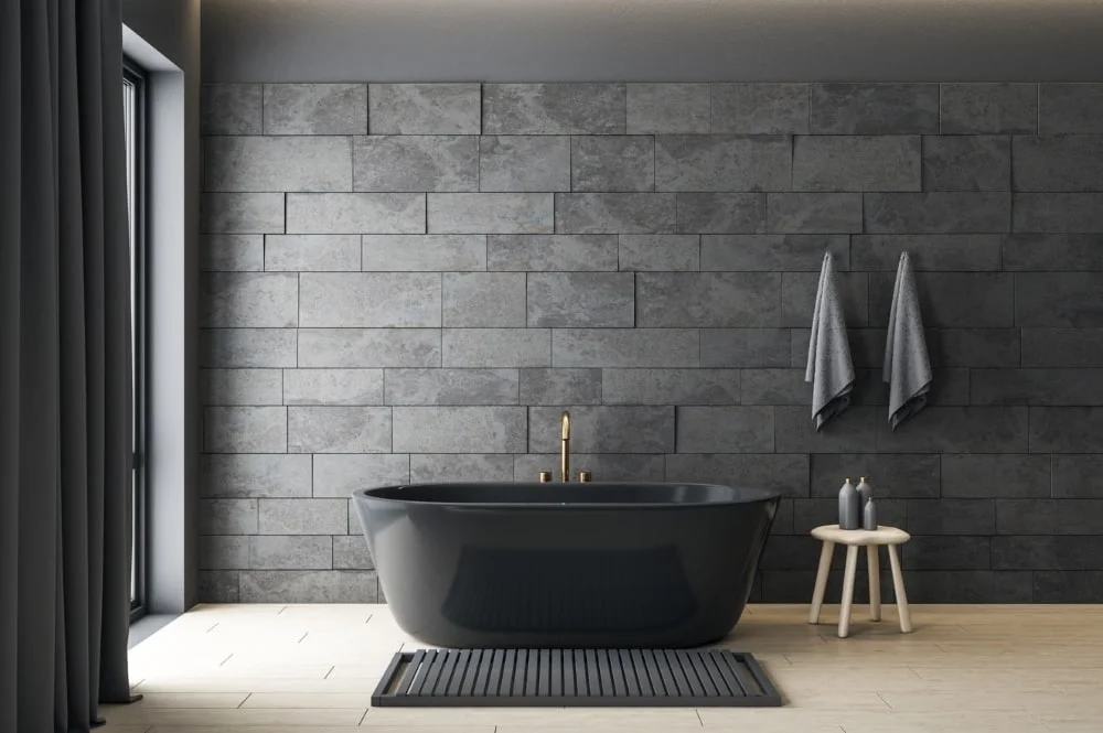 Schwarze Badewanne vor einer Wand aus grauen Fliesen.